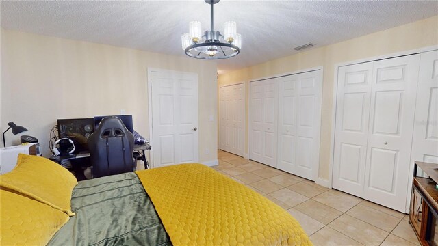 bedroom with a textured ceiling, light tile patterned flooring, visible vents, and multiple closets