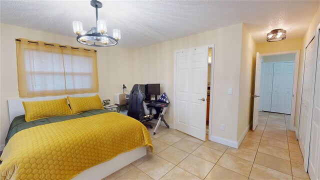 bedroom with a notable chandelier, a textured ceiling, baseboards, and light tile patterned floors