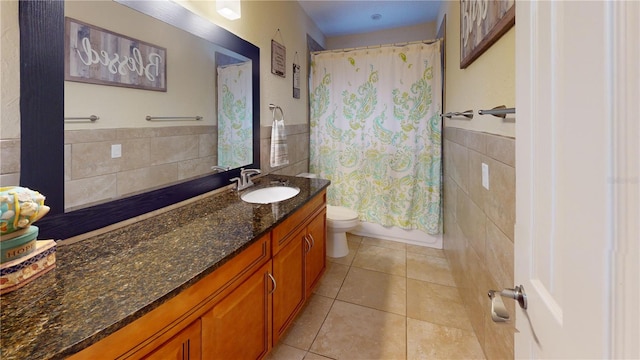 bathroom with toilet, a wainscoted wall, tile patterned flooring, vanity, and tile walls