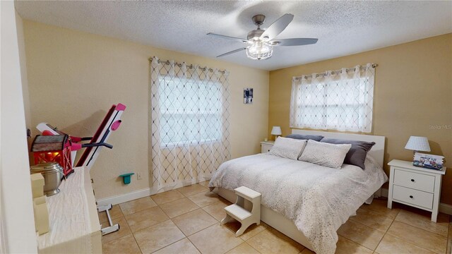 bedroom featuring light tile patterned floors, ceiling fan, baseboards, and a textured ceiling