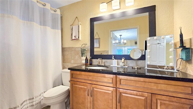 bathroom with toilet, curtained shower, vanity, and a textured wall