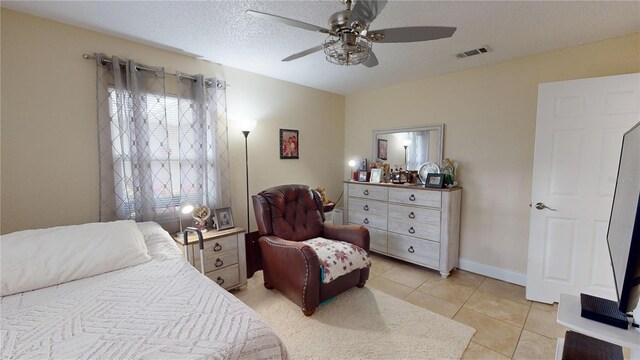 bedroom featuring light tile patterned floors, visible vents, a ceiling fan, a textured ceiling, and baseboards