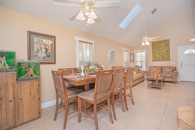 dining room with ceiling fan, light tile patterned floors, high vaulted ceiling, and a skylight