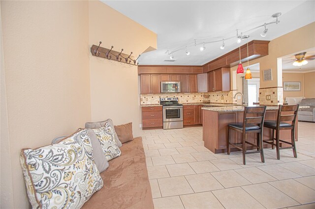 kitchen featuring kitchen peninsula, appliances with stainless steel finishes, tasteful backsplash, decorative light fixtures, and a breakfast bar area