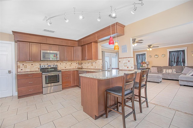 kitchen with light stone countertops, stainless steel appliances, kitchen peninsula, decorative light fixtures, and a kitchen bar