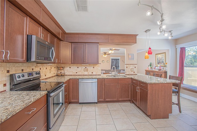 kitchen with kitchen peninsula, appliances with stainless steel finishes, a kitchen bar, sink, and decorative light fixtures