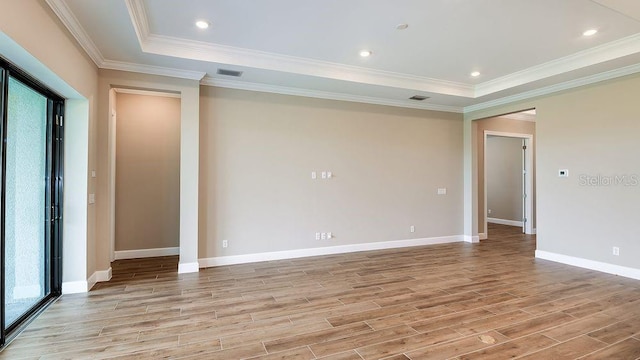 empty room featuring a raised ceiling, light hardwood / wood-style flooring, and crown molding