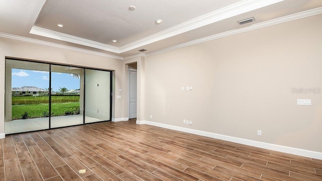 empty room with a raised ceiling, light hardwood / wood-style flooring, and ornamental molding