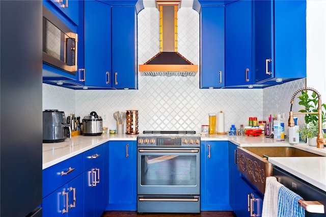 kitchen featuring wall chimney range hood, blue cabinets, and appliances with stainless steel finishes