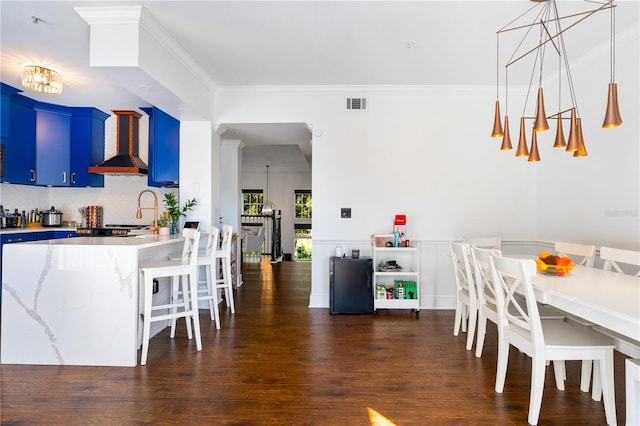 kitchen with blue cabinetry, wall chimney range hood, dark hardwood / wood-style floors, a chandelier, and decorative backsplash