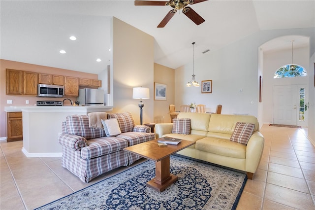 living room with ceiling fan with notable chandelier, light tile patterned floors, and high vaulted ceiling