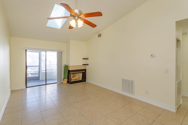 unfurnished living room with a skylight, ceiling fan, a fireplace, and light tile patterned floors