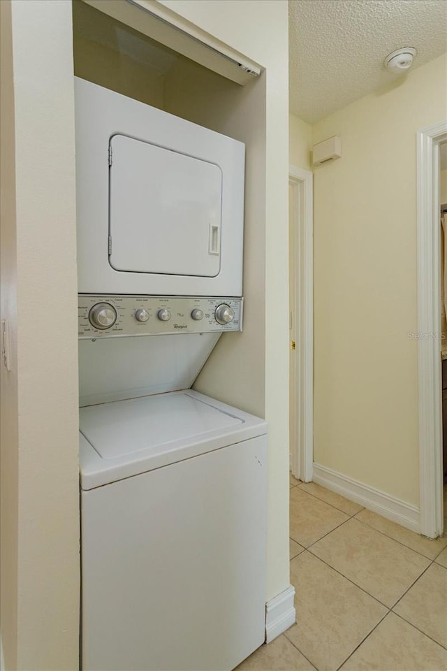 washroom with stacked washer / dryer, light tile patterned floors, and a textured ceiling