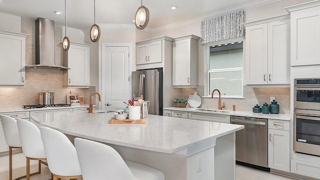 kitchen with wall chimney exhaust hood, sink, stainless steel appliances, and an island with sink