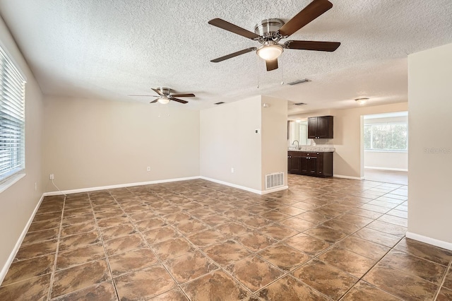 unfurnished living room with ceiling fan, sink, dark tile patterned floors, and a textured ceiling