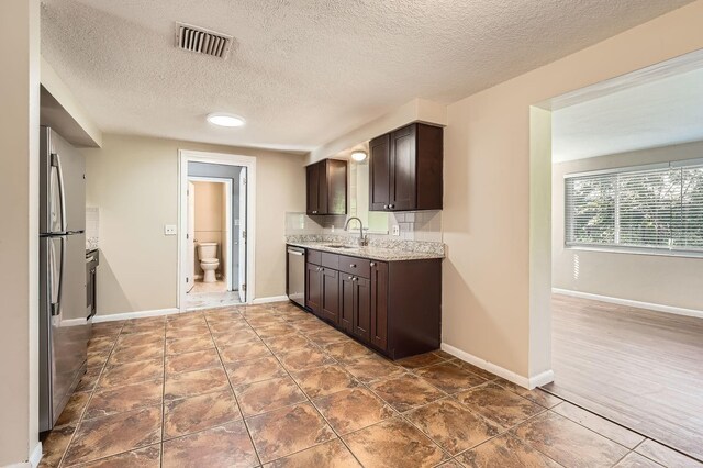 5023 Thames Dr, New Port Richey, FL 34652 - kitchen with appliances with stainless steel finishes, dark brown cabinets, a sink, a textured ceiling, and light stone counters