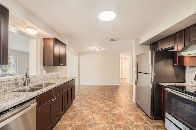 kitchen featuring light stone counters, dark brown cabinetry, stainless steel appliances, sink, and range hood