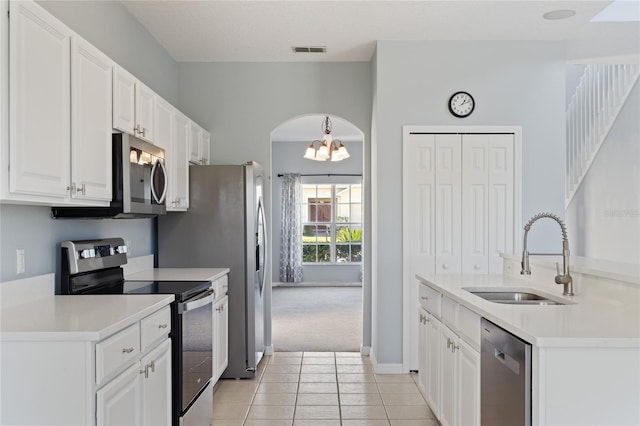 kitchen with an inviting chandelier, sink, appliances with stainless steel finishes, light tile patterned flooring, and white cabinetry