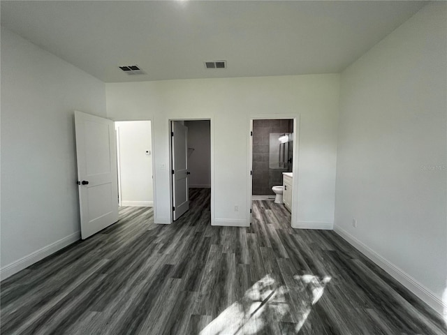 unfurnished bedroom featuring ensuite bath, a spacious closet, a closet, and dark hardwood / wood-style floors