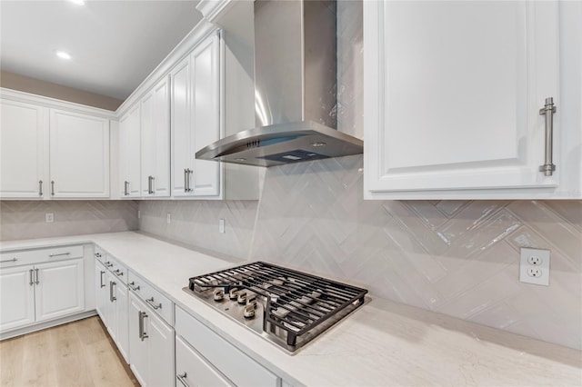 kitchen featuring stainless steel gas stovetop, white cabinetry, wall chimney range hood, and light hardwood / wood-style flooring