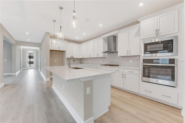 kitchen with white cabinets, sink, stainless steel appliances, and wall chimney range hood