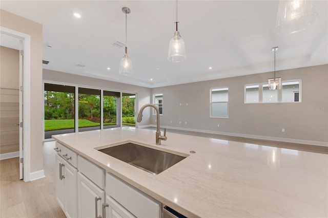 kitchen featuring light stone countertops, light wood-type flooring, sink, pendant lighting, and white cabinets