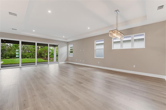 unfurnished living room featuring a tray ceiling, plenty of natural light, and light wood-type flooring