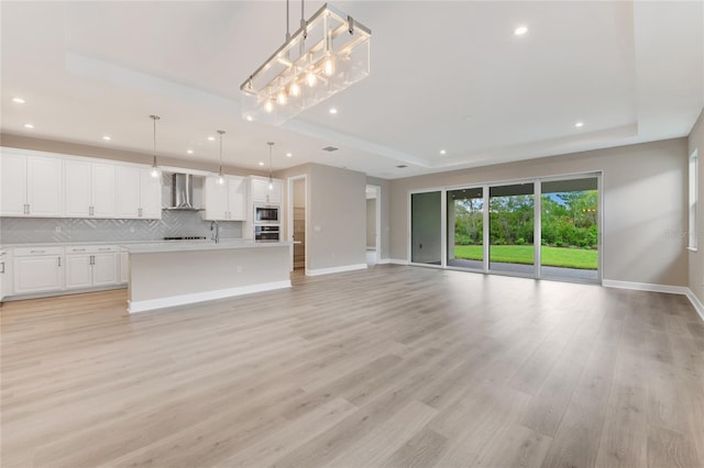 unfurnished living room featuring a raised ceiling, sink, and light wood-type flooring