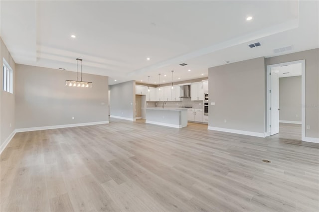 unfurnished living room featuring a tray ceiling, light hardwood / wood-style flooring, and sink