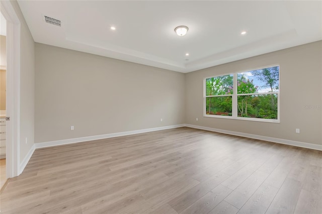 unfurnished room featuring a raised ceiling and light hardwood / wood-style flooring