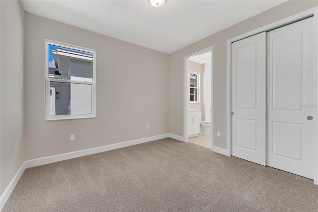 unfurnished bedroom featuring a closet, light carpet, and ensuite bath