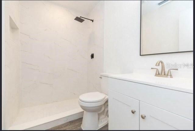 bathroom with vanity, toilet, and tiled shower