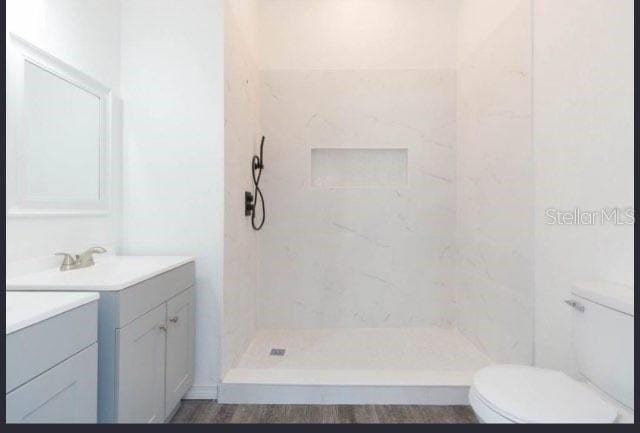 bathroom featuring a tile shower, vanity, toilet, and hardwood / wood-style floors