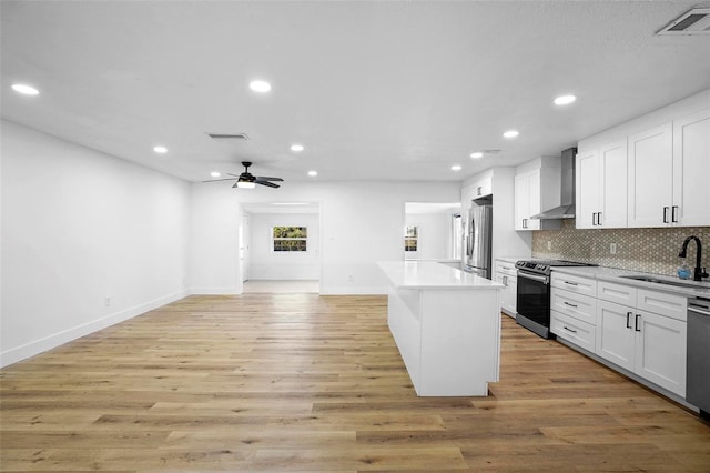 kitchen featuring wall chimney exhaust hood, stainless steel appliances, sink, white cabinets, and light hardwood / wood-style floors