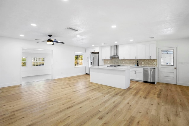 kitchen featuring light wood-type flooring, wall chimney exhaust hood, stainless steel appliances, a center island, and white cabinetry