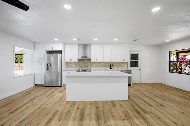 kitchen with white cabinets, appliances with stainless steel finishes, light hardwood / wood-style floors, and wall chimney range hood