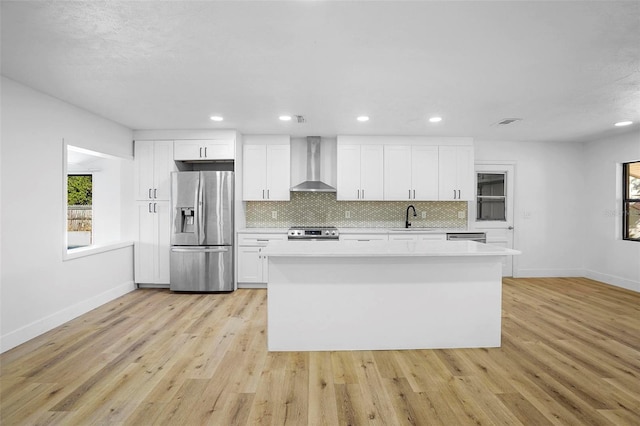 kitchen with white cabinets, stainless steel appliances, light hardwood / wood-style flooring, and wall chimney range hood