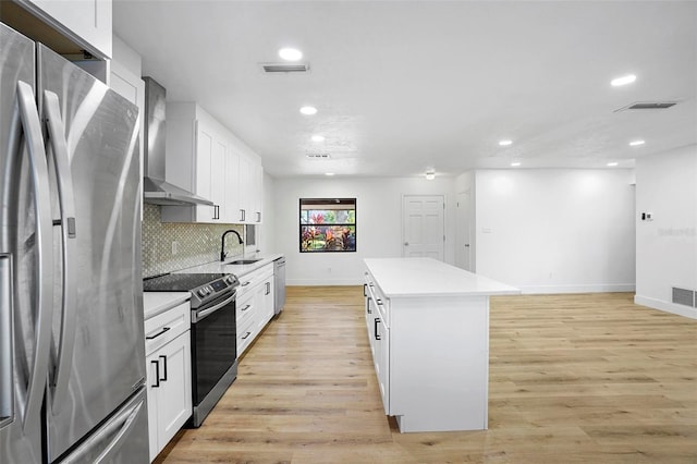 kitchen featuring wall chimney exhaust hood, a center island, appliances with stainless steel finishes, and light hardwood / wood-style flooring