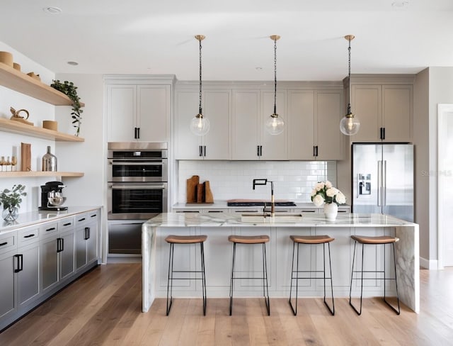 kitchen featuring light stone countertops, light wood-type flooring, a breakfast bar, a center island with sink, and gray cabinets