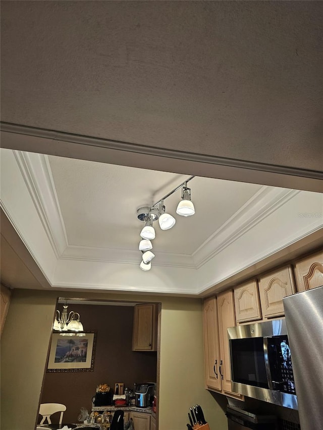 interior space with a raised ceiling, light brown cabinetry, a notable chandelier, and ornamental molding