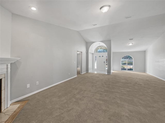 unfurnished living room featuring a tile fireplace, carpet floors, and vaulted ceiling