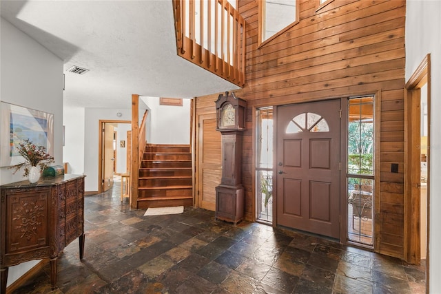 entrance foyer featuring a high ceiling, a textured ceiling, and wood walls