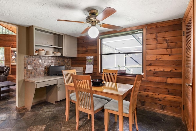 dining area with ceiling fan, a textured ceiling, and wooden walls