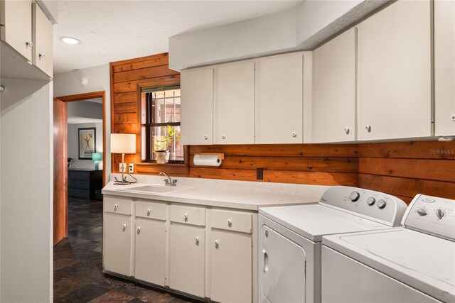 clothes washing area featuring washer and clothes dryer, wooden walls, sink, and cabinets