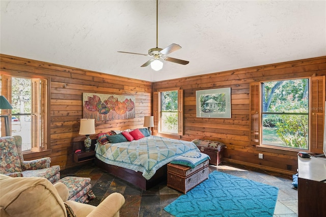 bedroom featuring a textured ceiling, multiple windows, wooden walls, and ceiling fan