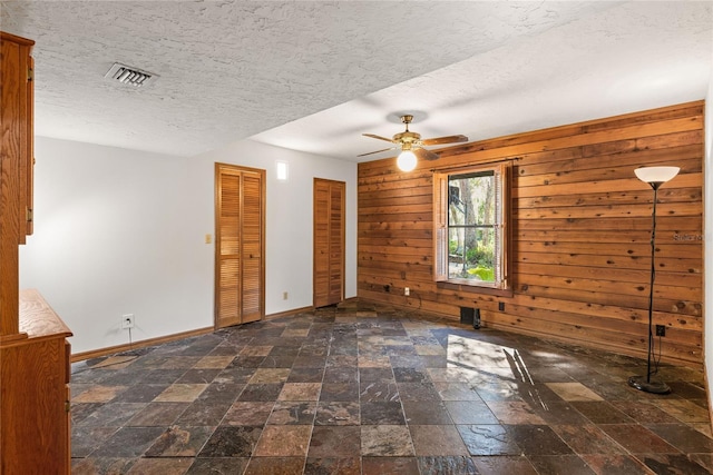 spare room featuring ceiling fan, a textured ceiling, and wooden walls