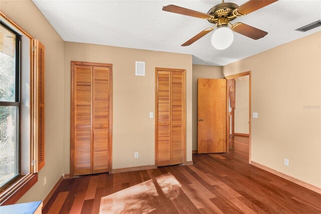 unfurnished bedroom with hardwood / wood-style flooring, two closets, and multiple windows