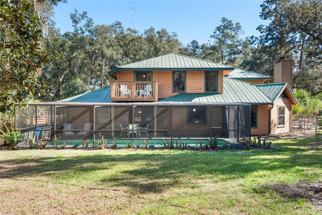 rear view of property featuring a lawn, a sunroom, a balcony, and a pool