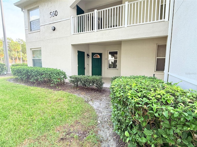 view of exterior entry with a lawn and a balcony