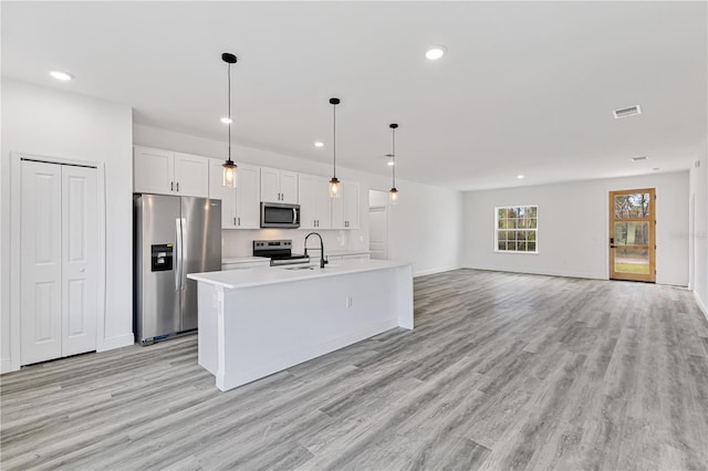 kitchen with appliances with stainless steel finishes, a center island with sink, decorative light fixtures, light hardwood / wood-style flooring, and white cabinetry